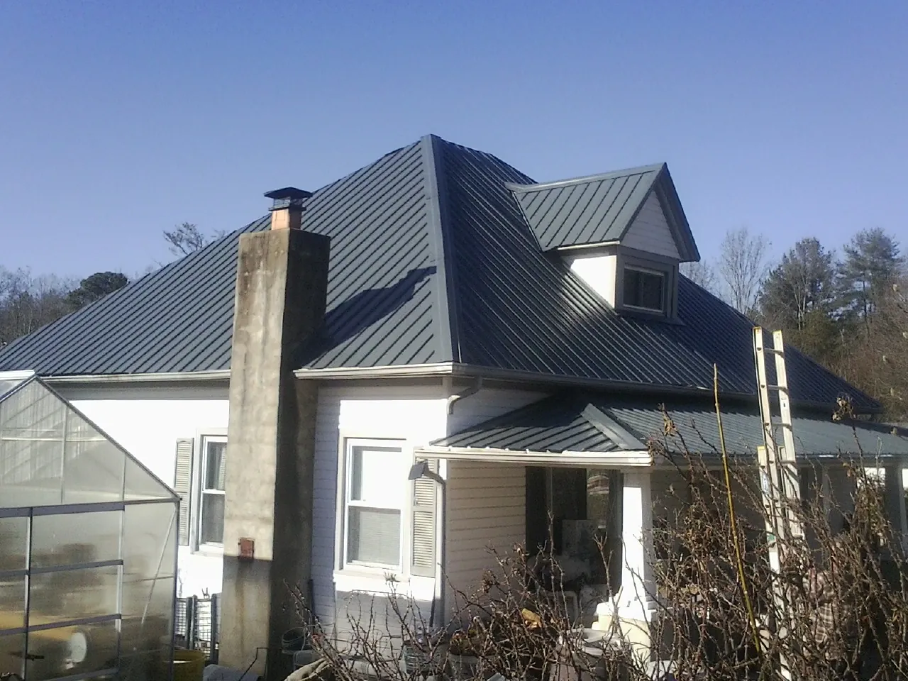 Dark blue standing seam metal roof on a white farmhouse with dormer — Slate & Tile Roof Repair by Roofing Brothers in Kings Park