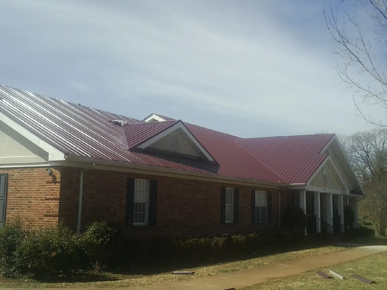 Red metal roof with gabled entries on a long brick building, from a Hail Damage Roof Repair job in Kings Park