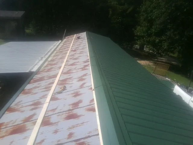 Old rusted panels beside newly installed green metal roofing — Wind Damage Roof Repair by Roofing Brothers in Kings Park
