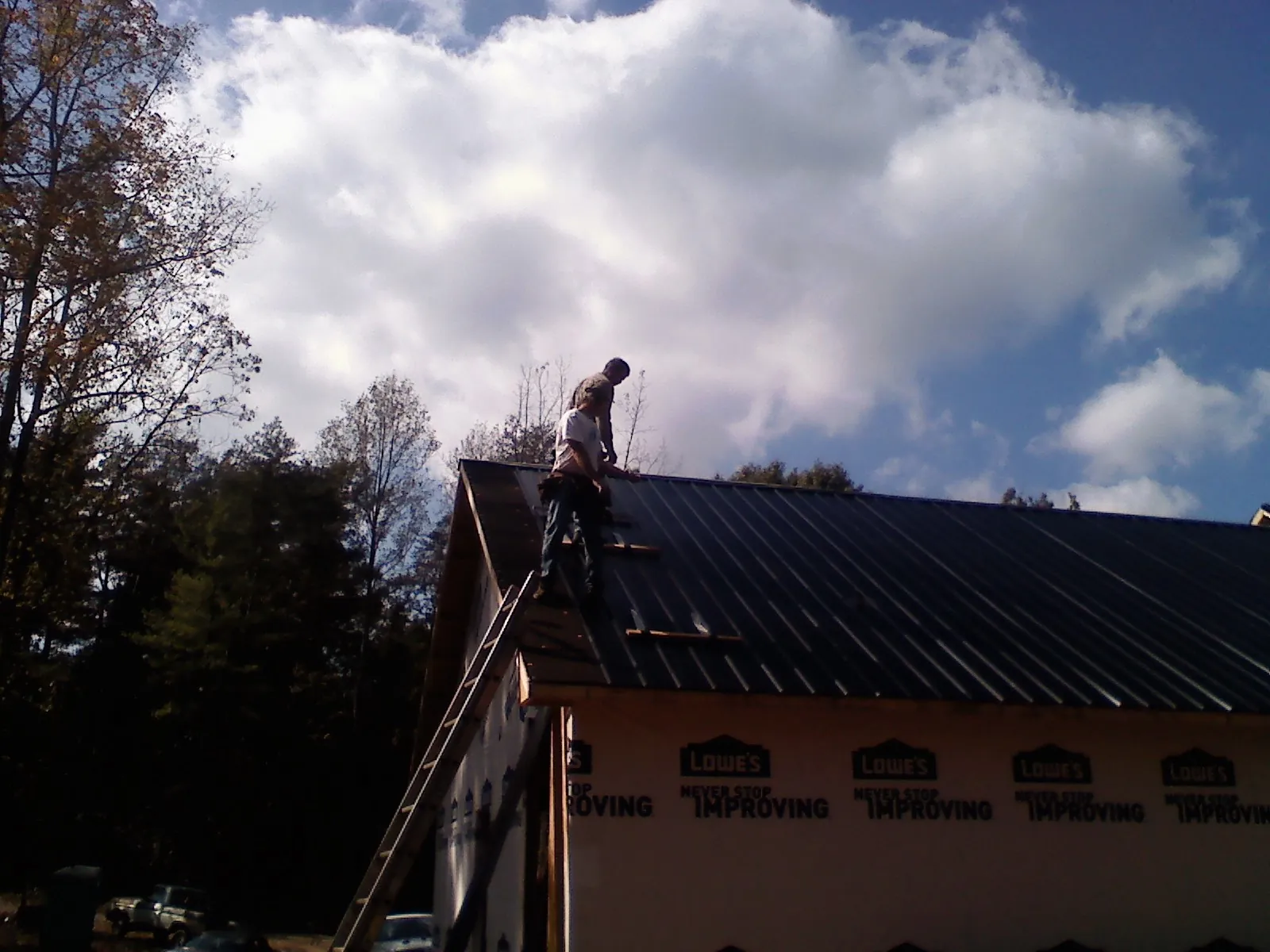 Roofer fastening dark metal panels high against a cloudy sky, from a Roof Inspection job in Kings Park