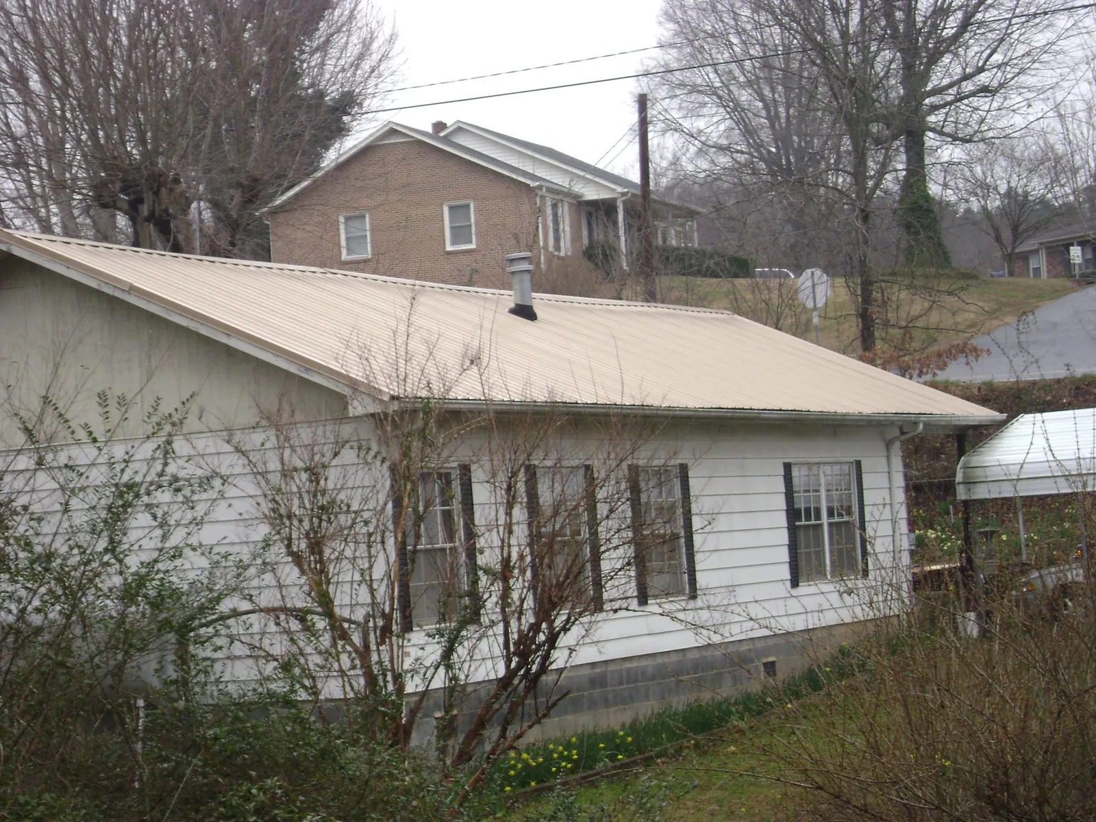 Tan metal roof on a white sided house set into a hillside — Commercial Roofing by Roofing Brothers in Kings Park