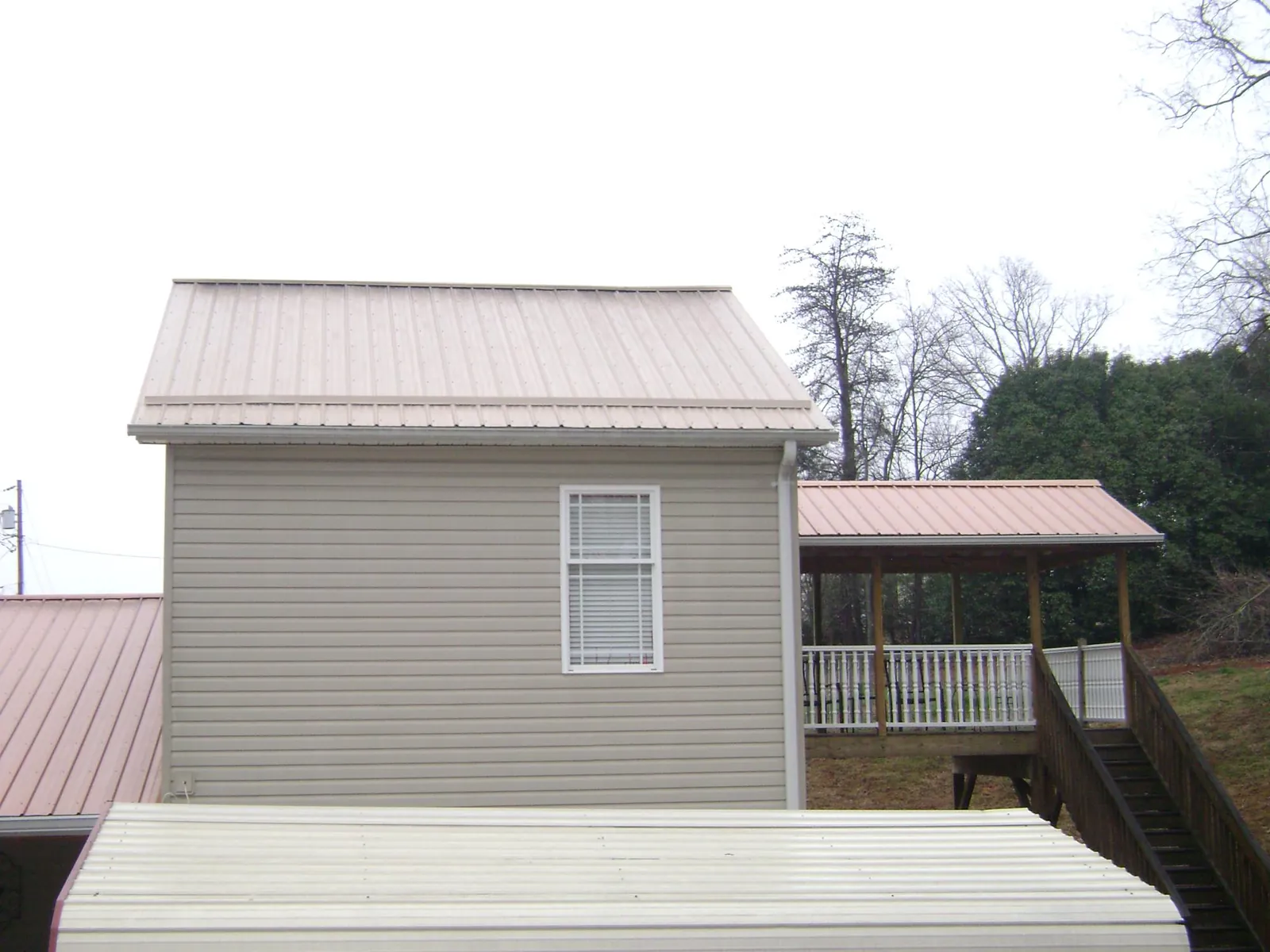 Tan metal roofs on a two story addition and attached porch, from a Roof Replacement job in Kings Park